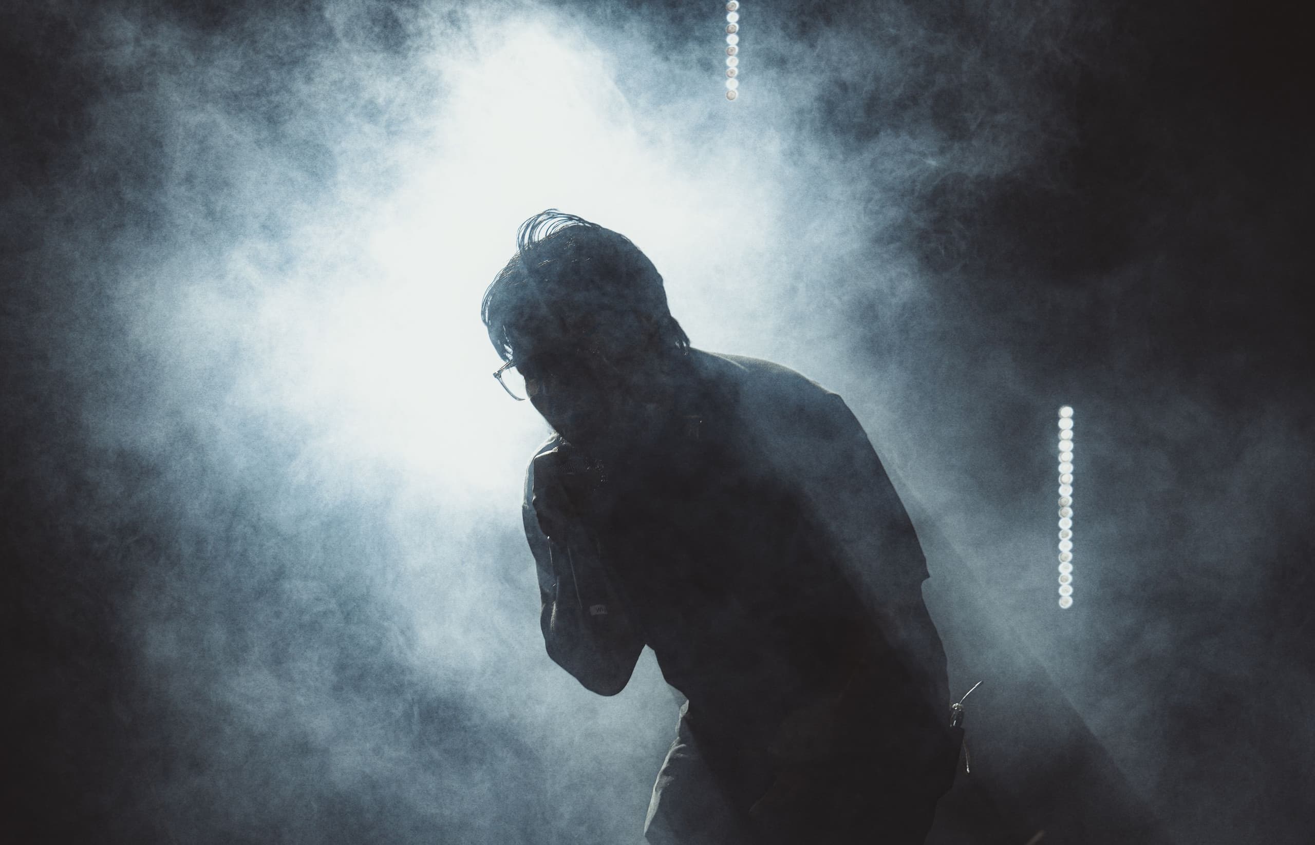 A performer bent over the microphone inside a wall of smoke